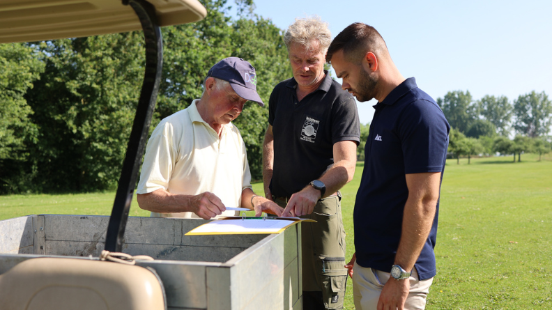 Three members of the trial team reviewing documents beside a golf buggy on the fairway at Golfcentrum de Batouwe.